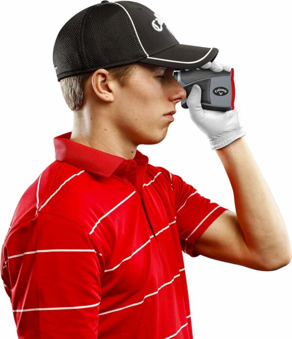 Person in red golf shirt and black cap using a golf rangefinder, wearing a white glove