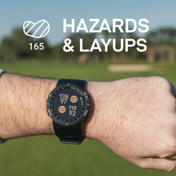 Close-up of a wrist wearing a golf GPS watch showing hazard and layup yardages, with a golf course and sand bunker in the background