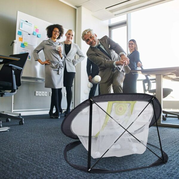 Office employees in a workspace playing indoor golf with a man swinging a club toward a practice net while others observe and laugh