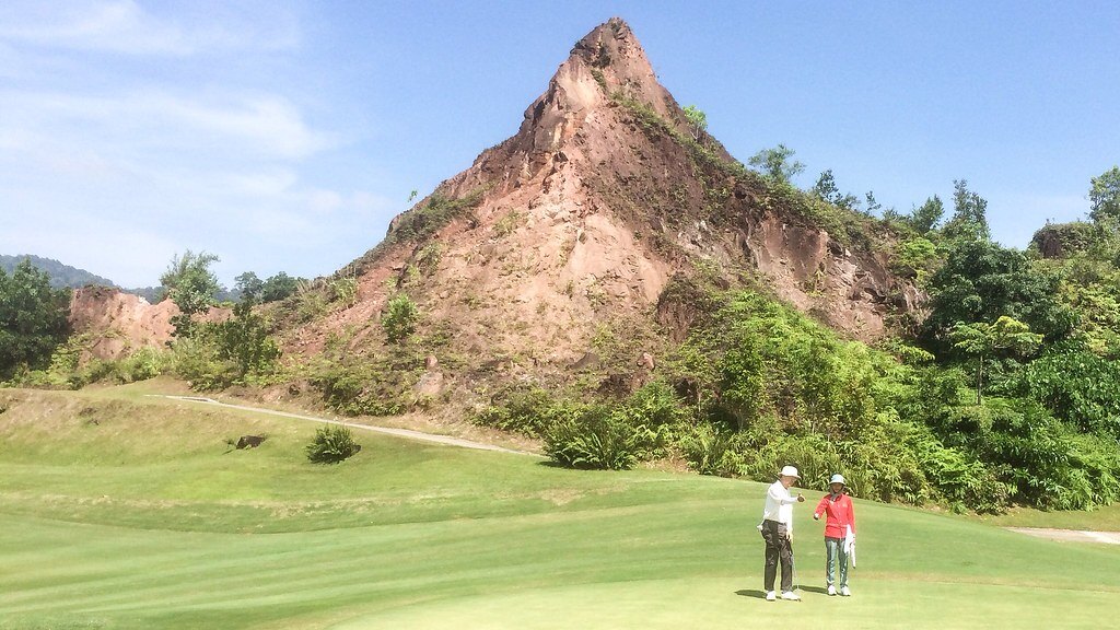 Golfers on a green below the red rock peak at Red Mountain Golf Club, Phuket