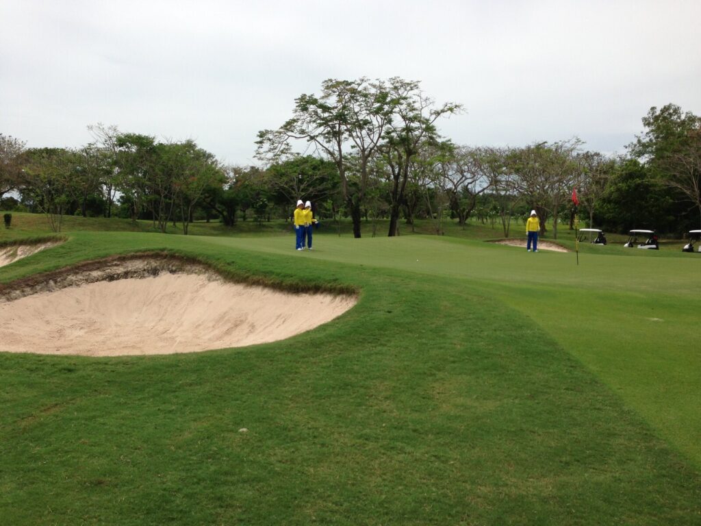 Caddies on a green at Siam Country Club Old Course in Pattaya with a deep sand bunker in the foreground